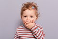 Shocked toddler. Astonished baby. Surprised infant little caucasian girl posing isolated over gray background covering mouth with Royalty Free Stock Photo