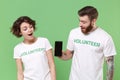 Shocked two young friends couple in white volunteer t-shirt isolated on green background. Voluntary free work assistance