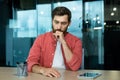 Shocked and upset young man sitting at the desk in the office, thoughtfully holding his head with his hand. Fired Royalty Free Stock Photo