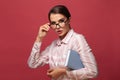 Shocked woman holding book touching her glasses and looking at camera on red banner background Royalty Free Stock Photo