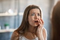 Shocked woman touching acne on her cheek while looking in mirror at home Royalty Free Stock Photo