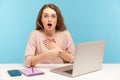 Shocked woman wearing eyeglasses and looking with open mouth in amazement, pointing at laptop screen Royalty Free Stock Photo