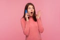 Shocked wondered woman with brown hair in pink sweater talking phone, listening to information with surprised expression, Royalty Free Stock Photo