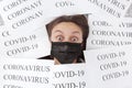 Shocked young beautiful woman in medical black mask lies in papers with inscription coronavirus and covid-19. Quarantine at home.