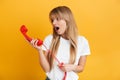 Shocked young blonde woman posing isolated over yellow wall background dressed in white casual t-shirt talking by telephone Royalty Free Stock Photo