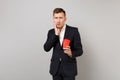 Shocked young business man in classic black suit putting hand on cheek holding paper cup with coffee or tea isolated on