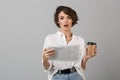 Shocked young business woman posing isolated over grey wall background reading newspaper drinking coffee Royalty Free Stock Photo