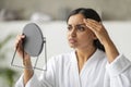 Shocked young eastern woman looking at mirror, touching her face Royalty Free Stock Photo