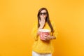 Shocked young girl in 3d imax glasses covering mouth with palm watching movie film holding bucket of popcorn isolated on