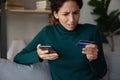 Shocked young latin lady using phone seeing bank card declined