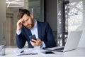 Shocked young man businessman, lawyer, banker sitting in office at desk, holding hand to head and looking frustrated at Royalty Free Stock Photo