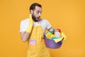 Shocked young man househusband in apron rubber gloves doing housework isolated on yellow wall background studio