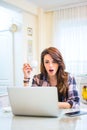 Shocked young woman holding coffee cup and looking at laptop. Royalty Free Stock Photo