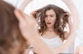 Shocked young woman holding her hair, looking at mirror