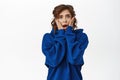 Shocked young woman, horrified, looking scared or worried, standing in blue hoodie over white background