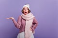 Shocked young woman in long knitted scarf standing on purple background with mouth open. Girl in trendy winter Royalty Free Stock Photo