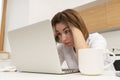 Shocked young woman sitting in the kitchen and working on laptop and counting spendings and taxes