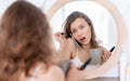 Shocked young woman talking on phone while putting mascara Royalty Free Stock Photo