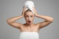 Shocked young woman wrapped in towel on grey background