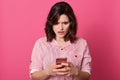 Shocking message concept. Surprised young darkhaired woman holding mobile phone and staring at its screen while standing against Royalty Free Stock Photo