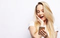 Surprised young blond hair woman holding mobile phone and staring at it while standing against white background. Royalty Free Stock Photo