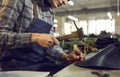 Shoe factory worker sitting at workshop table and using hammer to make leather boots Royalty Free Stock Photo