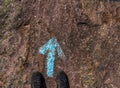 Shoes of a human standing at a blue painted direction arrow on the ground