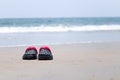 the shoes kept near the beach with waves of ocean are in the background