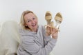 A woman in a tracksuit is dancing holding a pair of straw shoes with high thick heels in her hands. She is sitting on an Royalty Free Stock Photo