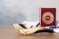 Shofar, Tallit and Torah book with text in Hebrew on wooden table indoors. Rosh Hashanah holiday attributes