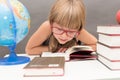 Shoolgirl reading a book at a table full of thick books and a globe Royalty Free Stock Photo