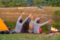 Shoot from back. A group of happy friends camping at riverside, dancing hold hands up  and enjoy view. Holidays fun Royalty Free Stock Photo