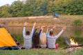 Shoot from back. A group of happy friends camping at riverside, dancing hold hands up and enjoy view. Holidays fun Royalty Free Stock Photo