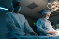 Shooting from below of male surgeon assisted by African female nurse in gown, mask and protective gloves using surgical Royalty Free Stock Photo