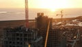Shooting from a drone under construction multi-storey building against the sunset, the builders walk on the roof