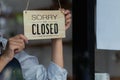 The shop owner puts a wooden sign that says it`s closed on the glass door of the shop to tell customers about the time it`s clos Royalty Free Stock Photo