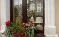 Shop window with dolls, figurines and lamps inside and a box with red and pink flowers outside.