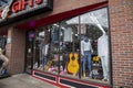 A shop window with mannequins displaying clothing, a large yellow guitar, pink stuffed animals and a neon open sign