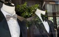 Shop window of mens tailor shop showing 2 mannequins in tuxedos.