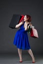 Shopaholic concept, young beautiful red-haired caucasian woman in blue dress posing in studio on gray background, professional Royalty Free Stock Photo