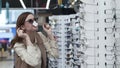 Shopaholic, stylish young woman shopper, buyer chooses sunglasses on shelves of store