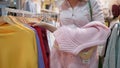 Shopaholism, happy girl chooses new clothes and hangs on hand for fitting in fashion store during discounts in mall