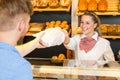 Shopkeeper in bakery hand bag of bread to customer