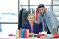 The shopkeeper and tailor reviews daily work on the table full of colorful fabrics and yarns