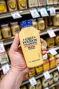 Shoppers hand holding a plastic container of grey poupon brand dijon mustard