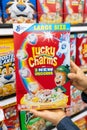 Shoppers hands holding a Package of General Mills Brand Lucky Charms frosted toasted oat cereal with marshmellows for sale