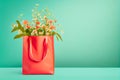 Shopping bag in living coral color with flowers bunch standing on table at turquoise wall background