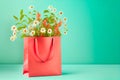 Shopping bag in living coral color with flowers bunch standing on table at turquoise wall background