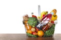 Shopping basket with grocery products on wooden table against white background Royalty Free Stock Photo