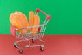 Shopping basket on a red and green background with plastic chicken and sausages inside. The concept of unnatural products with